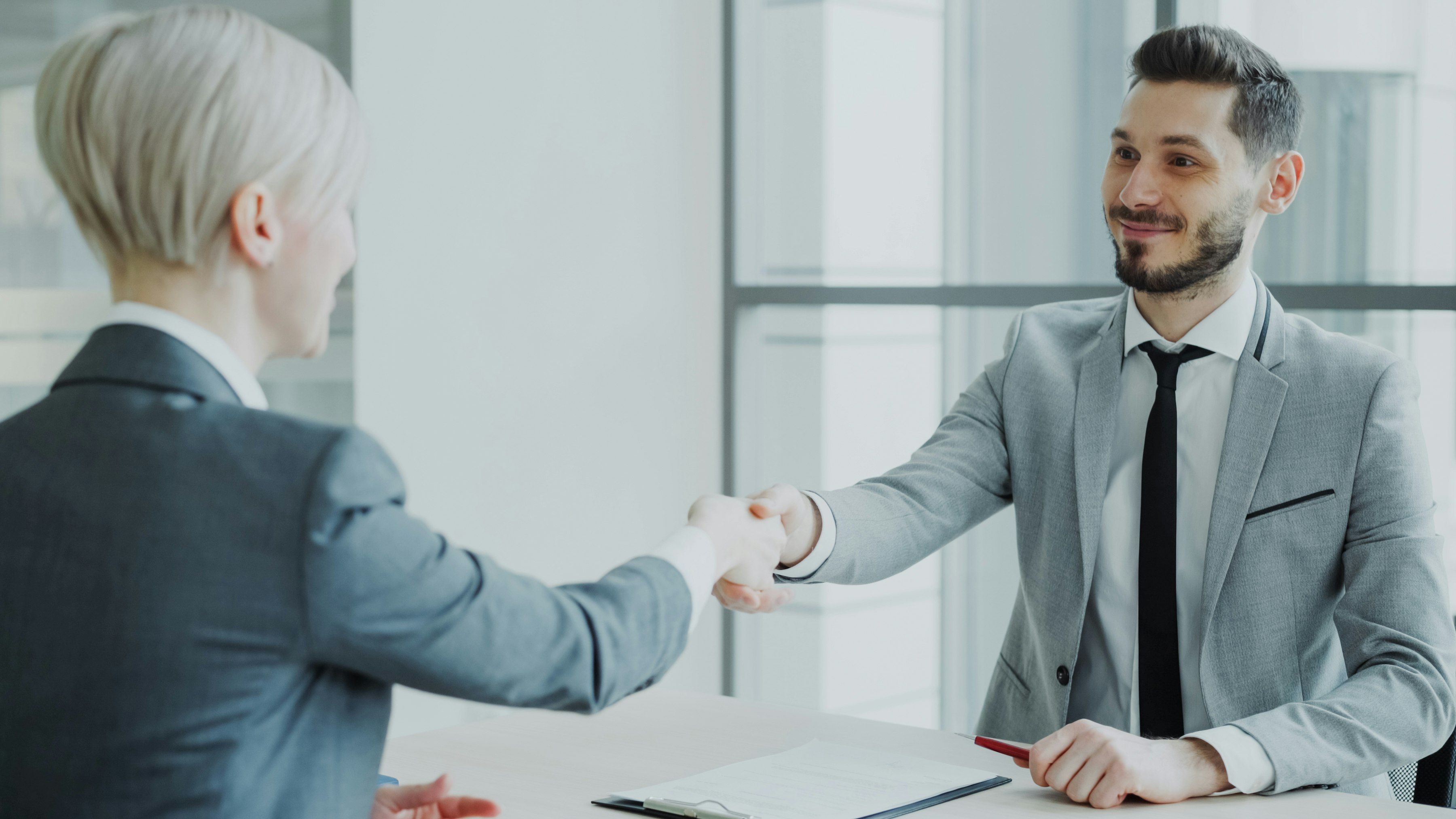 Une femme et un homme se serrent la main de part et d’autre d’un bureau.