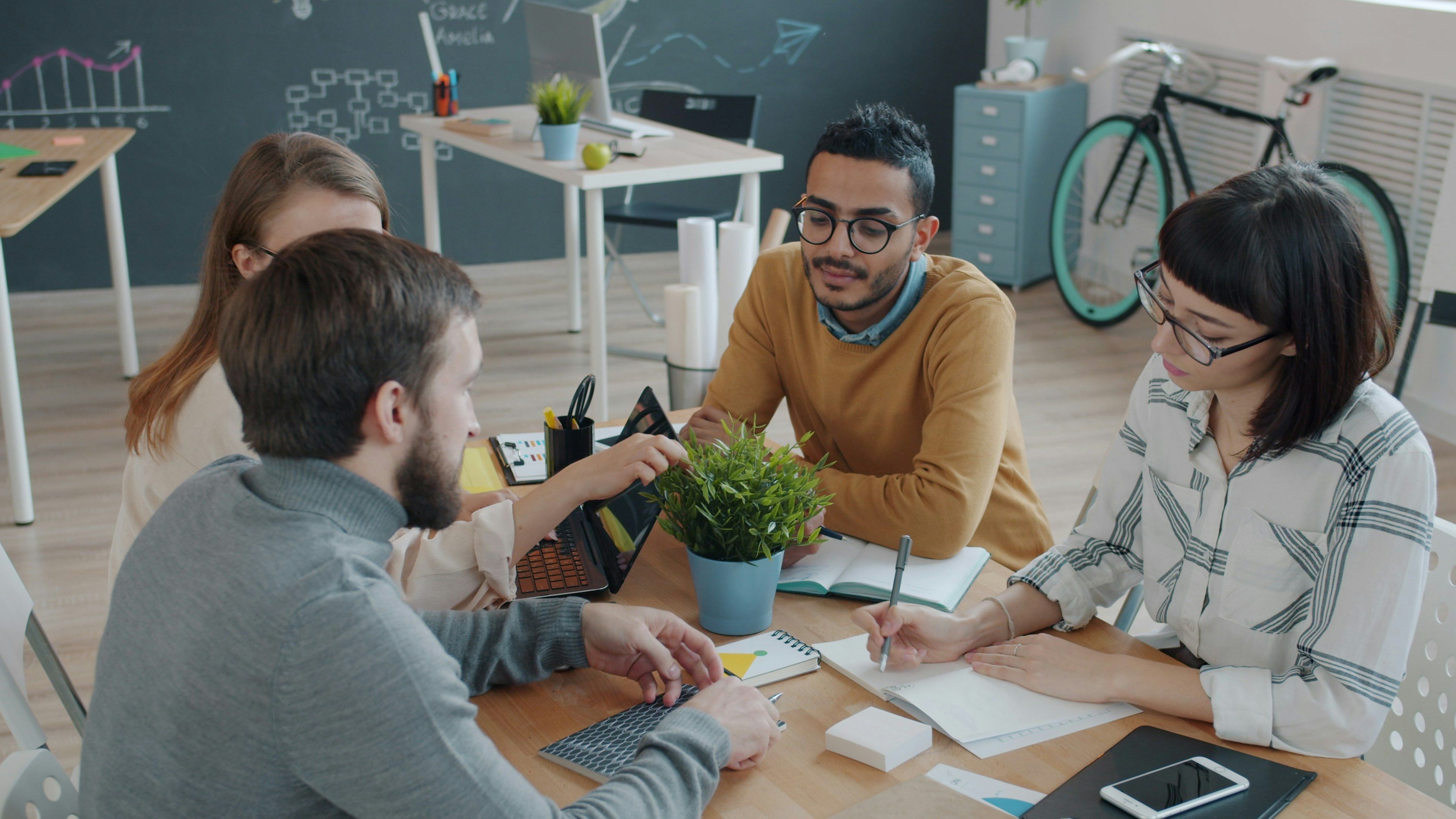 Une équipe travaille autour d’une table sur des ordinateurs portables, dans une ambiance détendue.