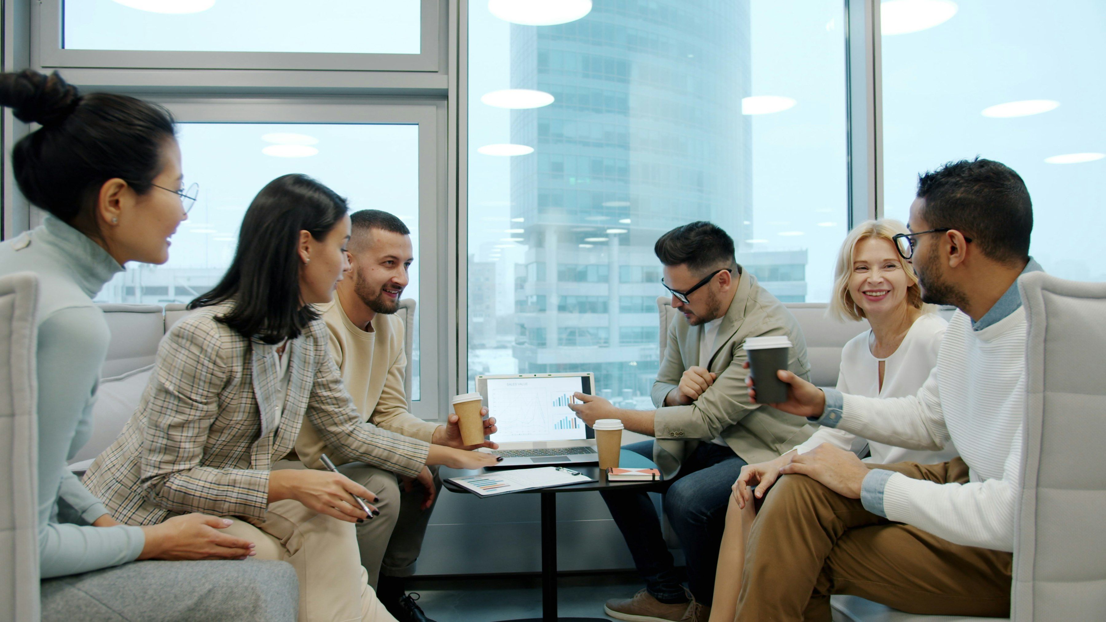 Une équipe de consultants échange de façon détendue autour d’une table basse, dans un salon de bureau lumineux.